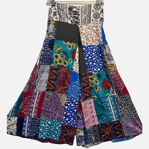 May include: A strapless, wide-leg jumpsuit with a patchwork design. The patchwork features various patterns and colors, including floral, polka dots, and paisley. The jumpsuit is hanging on a hanger against a white background.