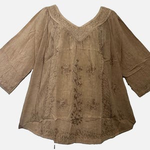 May include: A tan-colored tunic with three-quarter length sleeves and a V-neckline. The garment features intricate tonal embroidery in floral and vine patterns along the neckline, down the center front, and across the sleeve cuffs.