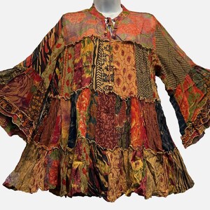 May include: A long-sleeved tunic featuring a multi-colored patchwork design with various floral, geometric, and animal print patterns. The garment has a tiered, ruffled silhouette, a round neckline with a tie closure, and flared sleeves.