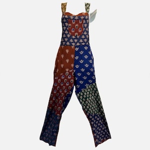 May include: A patchwork jumpsuit with a variety of patterns and colors. The top is a mix of navy blue and rust-colored fabric with floral designs. The pants are divided into sections of rust, navy, green, and blue, each with unique patterns.