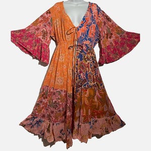 May include: A midi-length dress featuring a vibrant patchwork design with orange, pink, and blue floral and paisley patterns. The garment has a deep V-neckline with tie closures, wide bell sleeves, and a flared skirt with a ruffled hemline.