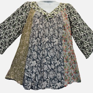May include: A V-neck tunic top featuring a patchwork design with various floral and botanical patterns in shades of olive green, charcoal gray, white, and soft pink. The garment has three-quarter length sleeves and a loose, flowing silhouette.