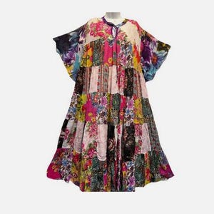 May include: A patchwork dress featuring a variety of floral patterns in pink, yellow, blue, and green. The dress has a tiered skirt and wide sleeves. The neckline is a keyhole design with a tie closure. The dress is displayed on a mannequin.