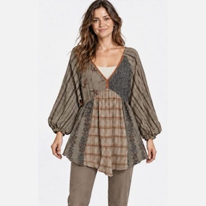 May include: A long-sleeved tunic featuring a V-neckline and a patchwork design. The garment combines olive green striped fabric, a brown plaid panel, a dark gray textured section, and floral embroidery accents. It has loose, gathered sleeves.