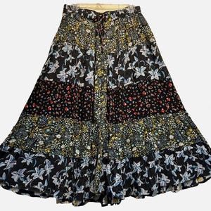 May include: A long, tiered skirt with a patchwork design. The skirt features various floral patterns in black, white, red, yellow, and blue. The skirt has a drawstring waist and a flowing silhouette, perfect for a bohemian style.