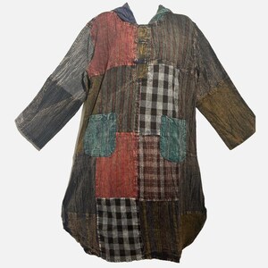 May include: A long-sleeve hooded tunic featuring a patchwork design with various fabric patterns including black and white gingham, red plaid, and solid textured panels in shades of brown, gray, and teal, with two front pockets and button closures.