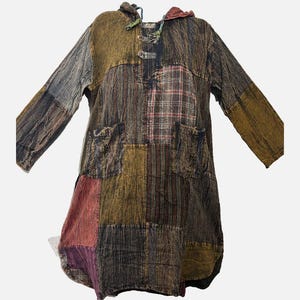 May include: A long-sleeved hooded tunic featuring a patchwork design in various earth tones including brown, olive, and maroon. The garment includes two front pockets, a drawstring hood, and a button-up placket at the neckline with textured fabric.
