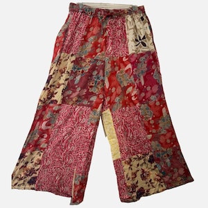 May include: Wide-leg pants featuring a patchwork design with various red, pink, and cream floral and paisley patterns. The garment has an elastic waistband with a drawstring tie at the center and a loose, flowing silhouette with a cropped length.