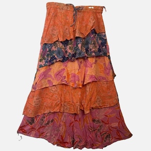May include: A tiered maxi skirt featuring a vibrant mix of orange, pink, and dark blue floral patterns. The skirt has an elasticized waistband with a drawstring tie and is constructed with multiple overlapping fabric layers that create a full silhouette.