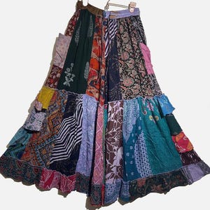May include: A patchwork skirt with a variety of patterns and colors, including floral, geometric, and striped designs. The skirt has a ruffled hem and is made of different fabric pieces sewn together. The color palette includes shades of green, blue, red, and purple.