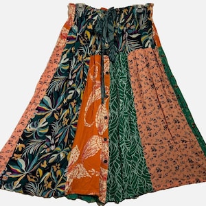 May include: A midi-length skirt featuring a patchwork design with various floral and leaf patterns in shades of orange, dark green, and peach. The skirt has an elasticized waistband with a tie closure and a vertical row of buttons down the front.