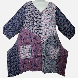 May include: A long-sleeve tunic featuring a patchwork design with various floral and geometric patterns in shades of navy blue, purple, white, and pink. The garment has a V-neckline, a front button closure, and two square patch pockets on the front.