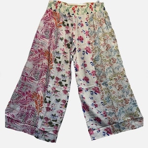 May include: Wide-leg pants featuring a patchwork design with various floral and botanical prints in shades of pink, blue, orange, and green on a white background. The pants have an elasticized waistband with a drawstring and a loose fit.