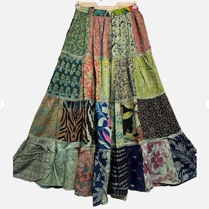 May include: A long, patchwork skirt with a tiered design. The skirt features a variety of fabric patterns and colors, including floral, animal print, and geometric designs. The skirt is hanging on a hanger.