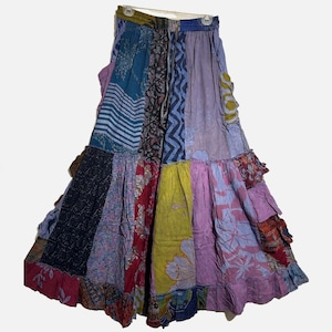 May include: A patchwork skirt with a variety of colorful fabric panels. The skirt features a tiered, ruffled design and a drawstring waist. The fabrics include floral, geometric, and abstract patterns in shades of blue, purple, red, and yellow.