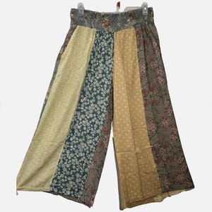 May include: Wide-leg pants featuring a patchwork design with vertical panels in varying floral and geometric patterns. The color palette includes shades of yellow, dark teal, and muted brown with pink floral accents. The pants have an elasticized waistband.