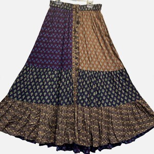May include: A long, flowing skirt with a patchwork design. The skirt features panels of burgundy, brown, and navy blue fabric, each with a different floral pattern. It has a button-up front and a ruffled hemline, creating a bohemian aesthetic.