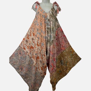 May include: A sleeveless jumpsuit featuring a patchwork design with various floral and paisley patterns in shades of peach, dusty pink, brown, and muted blue. The garment has a V-neckline, tie-up shoulder straps, and a wide-leg, loose-fitting silhouette.