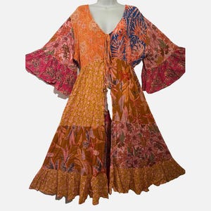 May include: A long-sleeved duster featuring a patchwork design with various floral and tropical leaf patterns in shades of orange, pink, yellow, and blue. The garment has a V-neckline, a front tie closure with wooden beads, and ruffled sleeve cuffs.
