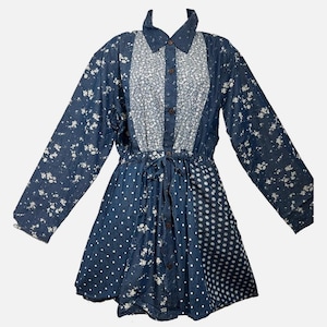 May include: A long-sleeved button-down dress featuring a patchwork design of dark blue denim fabric with white floral and polka dot patterns. The garment includes a collared neckline, a central button placket, and a drawstring waist tie.