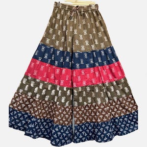 May include: Wide-leg palazzo pants with a drawstring waist. The pants feature a patchwork design with brown, navy, and pink panels. Each panel is decorated with white floral and paisley patterns. The pants are hanging on a white hanger.