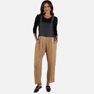May include: A black long-sleeve shirt worn under a pair of overalls. The overalls feature a dark charcoal denim bib top and tan-colored pants with a subtle repeating geometric pattern, side pockets, and a relaxed fit with a straight leg cut.