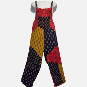 May include: A patchwork jumpsuit in red, navy, and yellow with floral patterns. The jumpsuit features adjustable straps and wide legs. The fabric appears to be lightweight, suitable for warm weather.