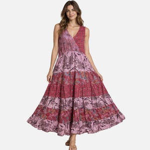 May include: A sleeveless maxi dress featuring a V-neckline and a tiered, flared skirt. The garment is constructed from panels of fabric in varying shades of pink, magenta, and lavender, decorated with a repeating floral and botanical print pattern.