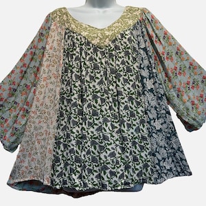 May include: A loose-fitting blouse featuring a patchwork design of various floral patterns in shades of green, blue, white, and orange. The garment has a wide scoop neckline and long, flowing sleeves, with a textured fabric finish throughout.