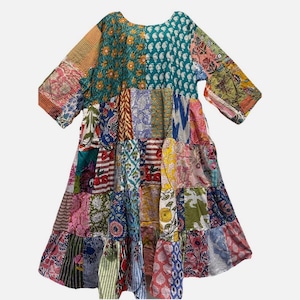 May include: A patchwork dress featuring a variety of colorful floral and geometric patterns. The dress has a round neckline, three-quarter sleeves, and a tiered skirt. The color palette includes teal, pink, yellow, and blue.