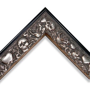 May include: An L-shaped corner section of a picture frame featuring a dark, weathered finish with raised, metallic silver-toned relief details. The decorative molding displays a repeating pattern of human skulls, blooming roses, and leafy vines.