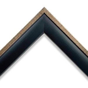 May include: A corner of a picture frame with a black interior and a gold-coloured, textured outer edge. The frame is angled, showcasing the contrast between the dark and light colours. The frame is set against a white background.
