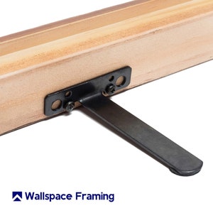 Puede incluir: Primer plano de un marco de madera con un caballete de metal negro. El caballete está unido al marco con tornillos. El marco está hecho de madera natural con un acabado marrón claro.