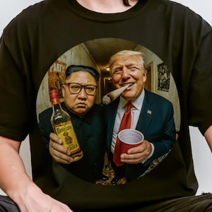 May include: Black t-shirt with a circular graphic of two men, one holding a bottle of alcohol and the other holding a red cup. The men are smiling and appear to be in a party setting. The text "PARTY" is visible in the background.