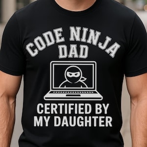 May include: Black t-shirt with white text that reads "Code Ninja Dad Certified by My Daughter". The text is in a rounded rectangle with a small image of a ninja inside a laptop.