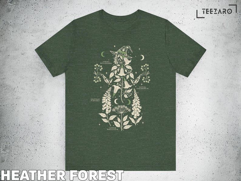Puede incluir: Camiseta verde bosque jaspeado con una ilustraci&oacute;n bot&aacute;nica de una figura de bruja. El dise&ntilde;o presenta varias plantas, lunas y estrellas, con etiquetas de texto. La camiseta tiene cuello redondo cl&aacute;sico y mangas cortas.