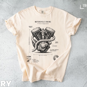 Puede incluir: Camiseta de color marfil con un diagrama detallado de un motor de motocicleta, etiquetado como "Motorcycle Engine V-Twin Configuration". El gráfico incluye medidas en cm y varios componentes del motor. La camiseta está hecha de un material suave y cómodo.