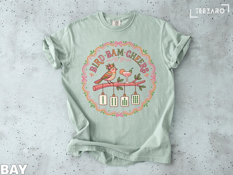 Bird and cocktail with "BAM CHEERS" text on a pale green t-shirt.