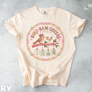 Cream t-shirt with "Bird Bam Cheers" graphic of a bird and cocktail.