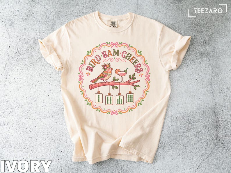 Cream t-shirt with "Bird Bam Cheers" graphic of a bird and cocktail.