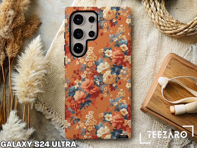 May include: A floral phone case for the Galaxy S24 Ultra. The case features a vintage floral pattern with orange, yellow, and blue flowers on a brown background.