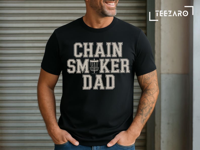 May include: Black t-shirt with the text "Chain Smoker Dad" in white letters with a disc golf disc icon in the middle of the text.