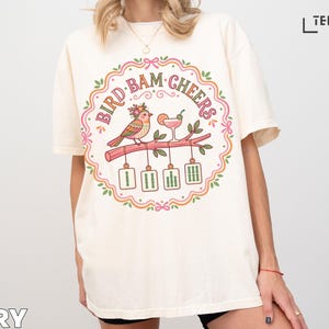 Cream t-shirt with "BIRD BAM CHEERS" text and bird on branch graphic.