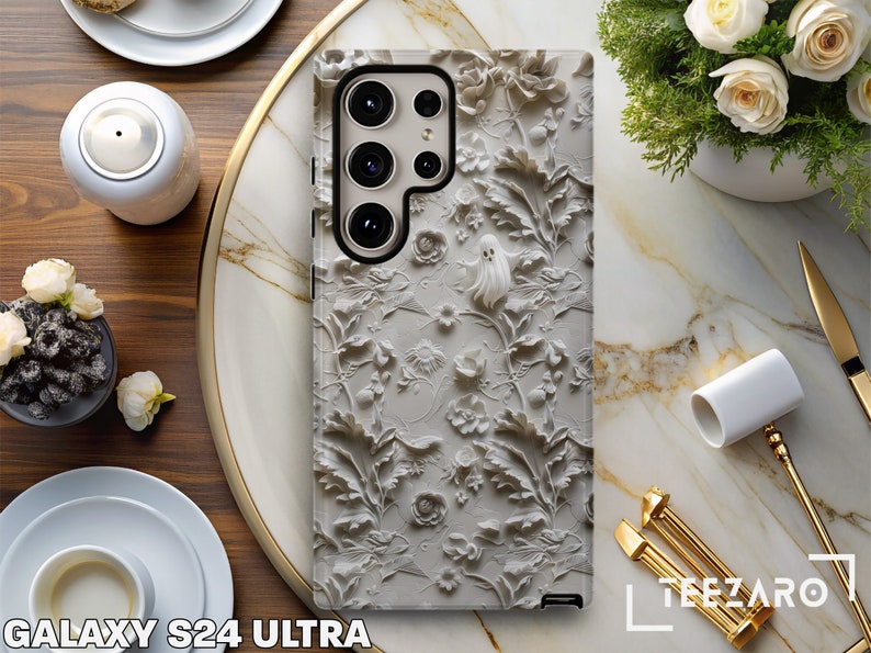 Puede incluir: Una funda de tel&eacute;fono blanca con un dise&ntilde;o en relieve 3D de flores y un fantasma. La funda est&aacute; dise&ntilde;ada para el Galaxy S24 Ultra.