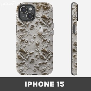 Puede incluir: Una funda blanca para iPhone 15 con un dise&ntilde;o en relieve 3D de flores y hojas blancas. Un fantasma blanco se encuentra en el centro del dise&ntilde;o.