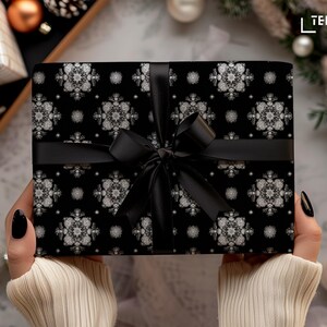 May include: A wrapped gift with black wrapping paper featuring a white snowflake pattern. The gift is tied with a black ribbon and bow. The overall theme is festive and suitable for the holiday season.