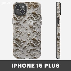 Puede incluir: Una funda para iPhone 15 Plus blanca con un dise&ntilde;o en relieve 3D de flores y hojas blancas. El dise&ntilde;o incluye una figura fantasmal en el centro.