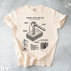 May include: Ivory-colored t-shirt with a detailed black and white diagram of a tuning lever and pin, labeled "TUNING LEVER AND PIN Acoustic Tension Regulation." The shirt features a crew neck and short sleeves.