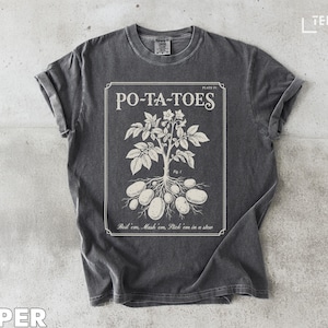 Puede incluir: Camiseta gris oscuro con un diseño blanco de una planta de patata y el texto "PO-TA-TOES". El diseño incluye la frase "Boil 'em, Mash 'em, Stick 'em in a stew."