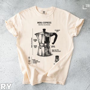 Puede incluir: Camiseta color marfil con un diagrama detallado de una cafetera Moka Express, con partes etiquetadas y medidas de 15-20 cm de altura. La camiseta incluye el texto "MOKA EXPRESS Machine macchinetta".